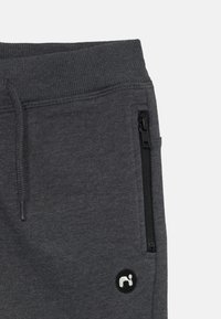 Gray sweatpants with a ribbed waistband, drawstring, side zipper pockets, and a circular logo patch in white on the lower leg.
