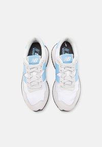 Bílé tenisky s světle modrými akcenty, které mají kombinaci síťoviny a semiše, ploché tkaničky a černou gumovou podešev.