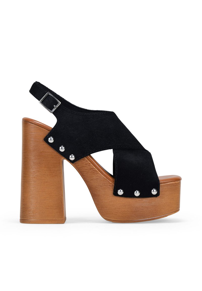 Sandalias de plataforma de ante negro con un tacón cuadrado y correa ajustable con hebilla. Presentan tachas plateadas a lo largo del costado y una suela con textura de madera.