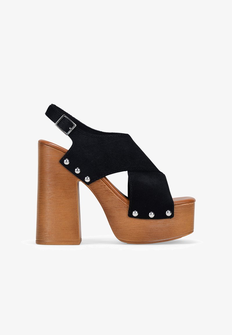 Sandalias de plataforma de ante negro con un tacón cuadrado y correa ajustable con hebilla. Presentan tachas plateadas a lo largo del costado y una suela con textura de madera.