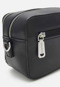 Black leather bag with a rectangular shape, silver zipper, and branded hardware tag. Features a side handle and smooth texture.
