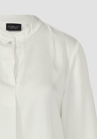 Weiße Bluse mit Stehkragen, versehen mit einem kleinen dekorativen Knopf am Ausschnitt. Glatte Stoffstruktur, maßgeschneiderte Passform.