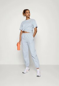 Conjunto atlético azul claro com um crop top atado e calças tapered, feito de tecido suave. Acompanhado por uma garrafa de água laranja.