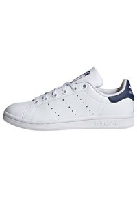 White leather sneaker with navy heel and tongue accents, round toe, perforated side design, and white rubber sole with branding detail.