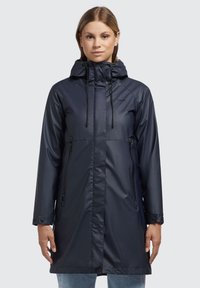 Chaqueta impermeable navy con cremallera frontal, capucha ajustable y bolsillos laterales. Presenta una textura suave y puños abotonados.