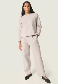 Lys grå sweater med lange ærmer, parret med matchende vide bukser og sorte flade sko. Glat tekstur, afslappet pasform, minimalistisk design.