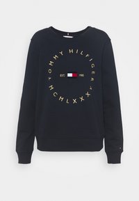 Sudadera navy con texto circular dorado, que presenta un pequeño detalle de bandera y "EST. 1985" en el centro. Fabricada con tejido de algodón suave.