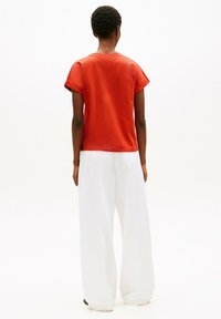 Czerwony t-shirt z krótkim rękawem i okrągłym dekoltem, zestawiony z luźnymi, białymi spodniami o szerokich nogawkach. Gładka faktura i swobodny krój widoczne od tyłu.