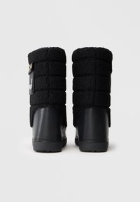 Um par de botas de inverno pretas com parte superior em fleece acolchoado e calcanhar em couro liso, exibidas por trás sobre um fundo branco.