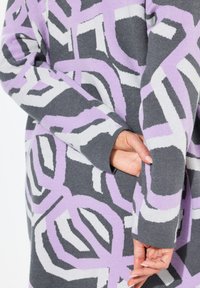 Grauer Pullover mit geometrischem Muster in Lavendel und Weiß. Mit langen Ärmeln und einer Tasche an der Seite, aus einem weichen Strickmaterial gefertigt.