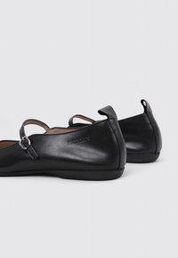 Zapatos planos Mary Jane de cuero negro con correas de hebilla, punteras redondeadas, suelas planas y una lengüeta en el talón, que muestran el nombre de la marca "wonders."