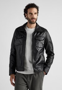 Zwarte leren jas met een ritssluiting aan de voorkant, puntige kraag en vier zakken. Het ontwerp heeft een gladde textuur en een getailleerde pasvorm.