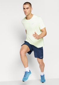 T-shirt Nike di un vivace giallo neon, pantaloni corti sportivi blu e scarpe da corsa blu. Maniche corte, collo tondo e logo Nike visibile su maglietta e scarpe.