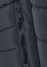 Mörk pufferjacka med en slät tygtextur, som har en svart dragkedja längs sidan och detaljer med quiltat mönster.