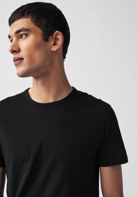 T-shirt in cotone nero con scollo rotondo, maniche corte e texture liscia. La vestibilità è aderente al corpo senza essere stretta.