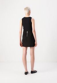 Haut noir sans manches associé à une mini jupe noire taille haute dotée d'une fermeture éclair centrale en argent et d'une tirette circulaire, avec une texture lisse.