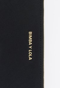 Czarny materiałowy worek z teksturą z wyszywanym na złoto logo "BIMBA Y LOLA", z złotym zamkiem błyskawicznym wzdłuż krawędzi.