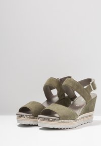 Olivgrön mocka kilklackssandaler med öppen tå, ankle straps och justerbar spänne, med en texturerad silverdetalj på sulan.