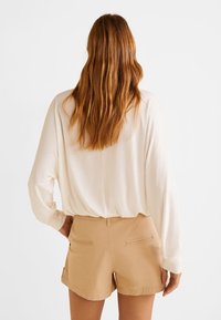 Top de manga larga beige claro con un ajuste holgado, combinado con pantalones cortos a medida de color marrón claro que cuentan con dos bolsillos traseros. Textura suave y lisa.