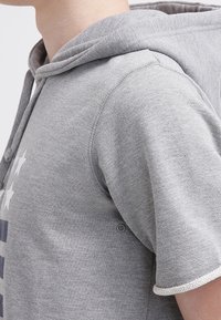 Sudadera gris con capucha con cordón, mangas cortas y dobladillo acanalado. Presenta detalles de costura sutiles y una textura suave y lisa.