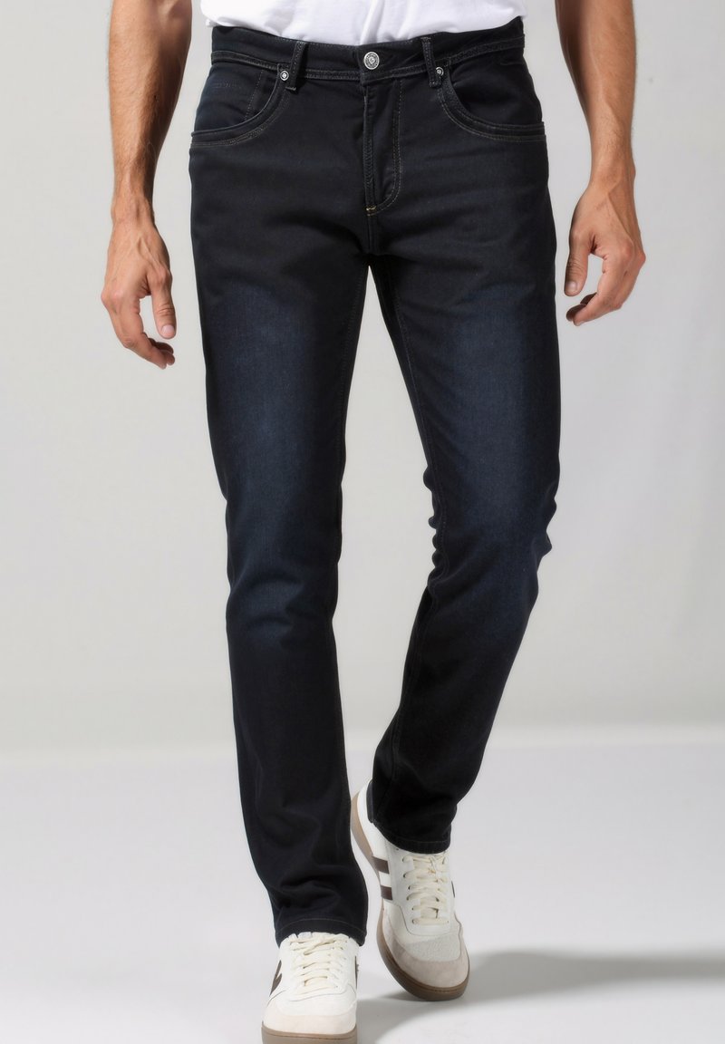 Jeans de mezclilla oscura con un corte ajustado, que cuentan con cinco bolsillos, costuras tonales y un brillo sutil. Combinados con zapatillas blancas.