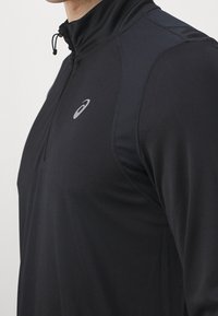 Czarny sportowy top z zamkiem ćwierć długości o gładkiej teksturze, z wysokim kołnierzem i małym logo na piersi, zaprojektowany z myślą o komforcie i swobodzie ruchów.