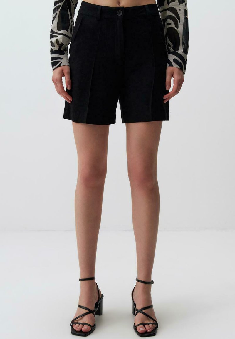 Pantaloni pantaloni neri a pieghe con vita aderente e chiusura con bottone. Tessuto liscio con design sartoriale. Abbinati a tacchi alti neri con cinturini.