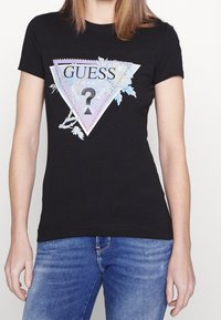 Czarny bawełniany t-shirt z trójkątną, kolorową grafiką z kwiatowymi akcentami i cekinami, z nazwą marki "GUESS."