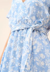 Vestido azul claro con patrón floral blanco, cinturón de tela atado en la cintura y escote en V.