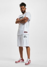 Hvit atletisk trøye og shorts med meshstruktur, med svart logo og nummer "05." Kombinert med røde og hvite joggesko.