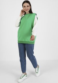 Zielony, oversize'owy top bez rękawów wykonany z bawełny, zestawiony z niebieskimi dżinsami i białymi trampkami z zielonymi akcentami. Prosty design i krój.