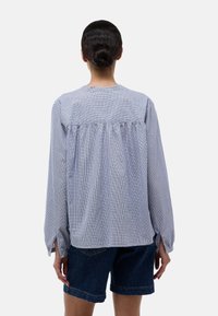 Chemise à manches longues à carreaux vichy bleu et blanc avec un détail froncé au dos, un col rond et des fentes sur les côtés, portée avec un short en denim.