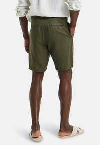 Olivengrüne Leinenshorts mit normalem Schnitt, versehen mit zwei Gesäßtaschen und feiner Textur, kombiniert mit hellen Sandalen.