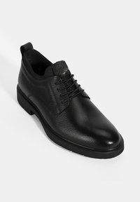 Chaussures en cuir noir avec une finition texturée, bout rond et design à lacets. Elles comportent une semelle en caoutchouc solide et un petit talon.