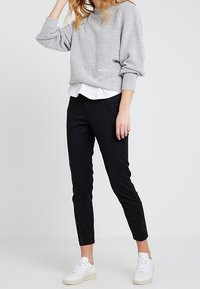 Grå, stickad tröja med lösa ärmar, kombinerad med svarta slim-fit byxor och vita sneakers. Lager på lager med en vit skjorta under.