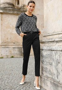 Zwart-wit gemêleerde blouse met lange mouwen, gecombineerd met op maat gemaakte zwarte trousers en witte block-heeled schoenen. Elegante, soepele texturen.