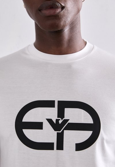 Tricou alb cu un logo grafic negru, ce prezintă literele „E” și „P” interconectate. Mâneci scurte și guler rotund. Textură netedă.