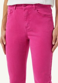 Dopasowane różowe dżinsy o gładkiej teksturze, z kieszeniami z przodu oraz średnim stanem. Zawierają zapięcie na guzik i szlufki na pasek.