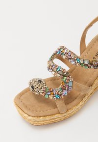 Bež espadrila sandal s dizajnom zmije ukrašenim dragim kamenjem, s raznobojnim kamenčićima i teksturiranim nubuk trakama. Platforma s tkanim detaljima.
