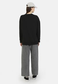 Černá oversize mikina s kulatým výstřihem, v kombinaci s širokými šedými džíny. Světlá šedá kšiltovka doplňuje celý outfit.