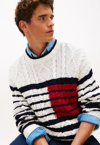 Ριγέ πουλόβερ με υφή πλεξίματος καλώδια σε λευκό, ναυτικό μπλε και κόκκινο. Διαθέτει ένα έντονο κόκκινο τετράγωνο και μανσέτες πουκάμισου από τζιν που προεξέχουν.