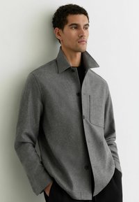 Grijze jas van een wolblend met een opstaande kraag, knoopsluiting aan de voorkant en een opgestikte zak aan de linkerkant. Gladde textuur en een ontspannen pasvorm.