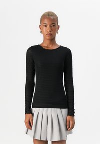 Top negro de manga larga con un patrón texturizado, escote redondo, silueta ajustada, combinado con una falda gris plisada.