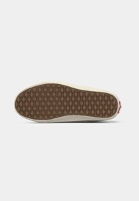 Chaussure unique retournée semelle vers le haut montrant un motif gaufré marron et hexagonal avec des côtés beige sur fond gris clair.