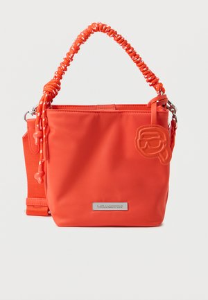 Μικρή φωτεινή πορτοκαλί τσάντα χειρός με πλεκτή λαβή, αποσπώμενο λουρί ώμου και πλακέτα με το λογότυπο της μάρκας μπροστά.
