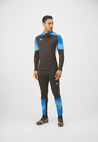 Sportoutfit mit einem schwarzen Langarmoberteil mit blauen Farbverlauf-Akzenten und passenden schwarzen Leggings, beide aus dehnbarem Material.