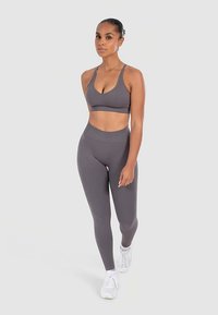 Reggiseno sportivo grigio e leggings a vita alta in tessuto elasticizzato. Modella con scarpe da ginnastica bianche; design minimalista, texture senza cuciture.