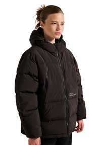 Sort puffer-jakke med hætte, lynlås foran og lommer, med struktureret stof og et trykt logo på brystområdet.