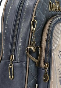 Zaino trapuntato blu e marrone con molteplici cerniere, charm a forma di cuore metallico e di spilla da balia, e accenti testurizzati in colori contrastanti.