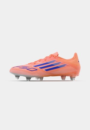 Chuteira de futebol laranja brilhante com riscas azuis. Apresenta um cabedal texturizado, fecho com atacadores e cravos de borracha transparente na sola.